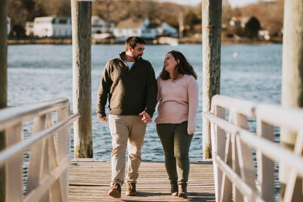 A couple walks on a dock while working on their Mystic engagement photos.