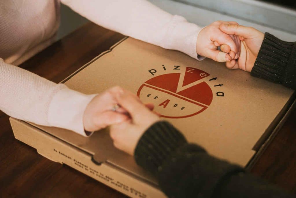 A man and woman hold hands on a pizza box during their winter Mystic engagement session.