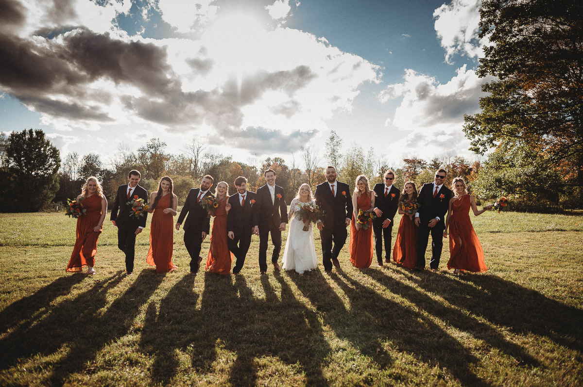 A wedding party of 12 bridesmaids and groomsmen plsu the bride and groom walk side by side in a silly way at a Connecticut farm wedding.