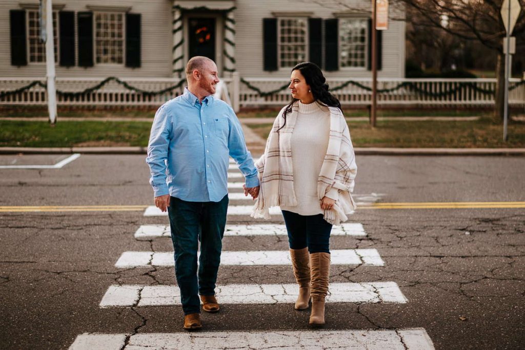 A couple holds hands and crosses the street in a crosswalk during their Wethersfield engagement session.