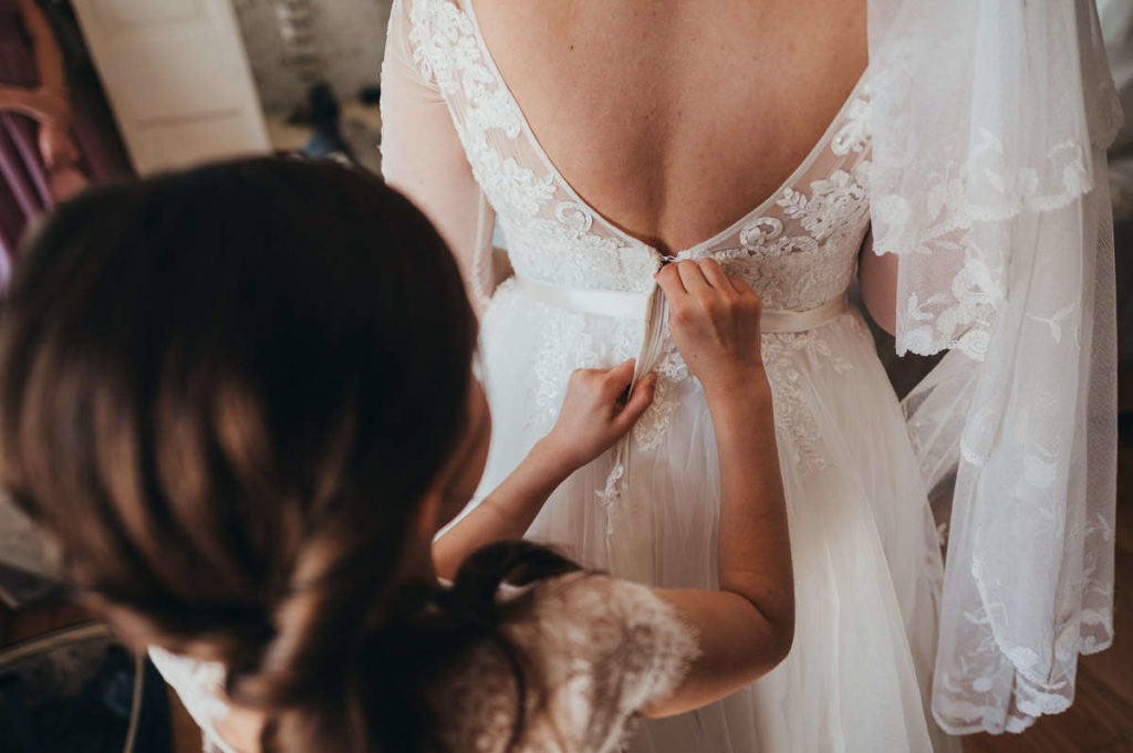 A bride has her wedding dress zipped up by her daughter during her Mystic, CT wedding.
