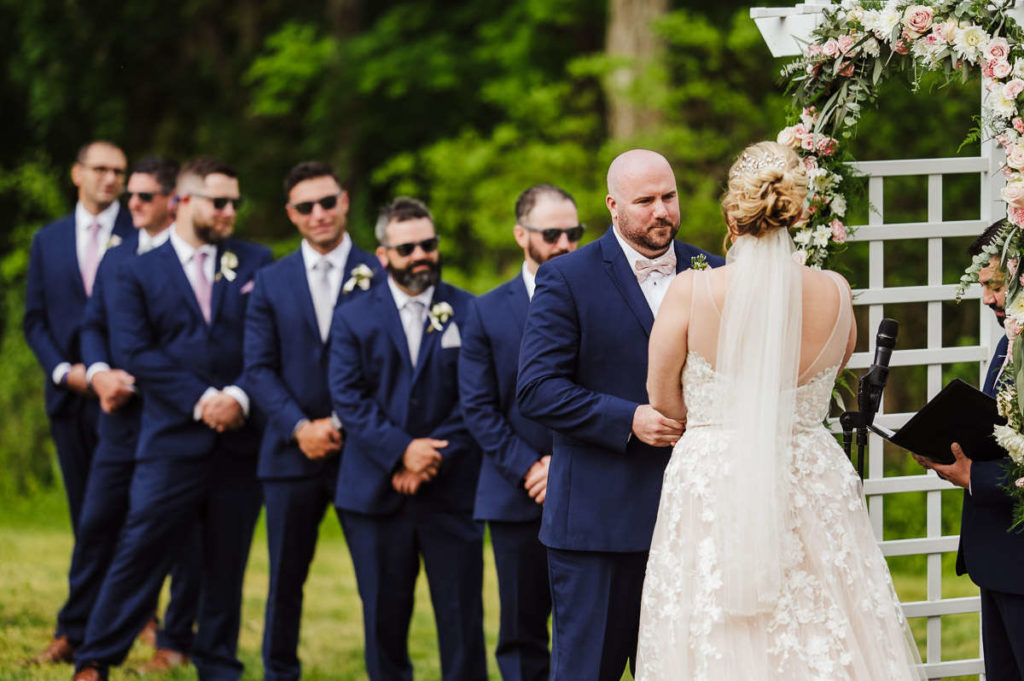 During their spring Mystic, CT wedding, a bride and groom hold hands at the altar while the groomsmen look on.