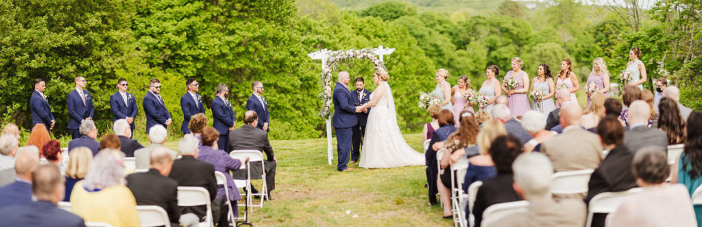 A ceremony during an Inn at Mystic wedding. The bride and groom stand in the center at the altar while their attendants and guests surround them.