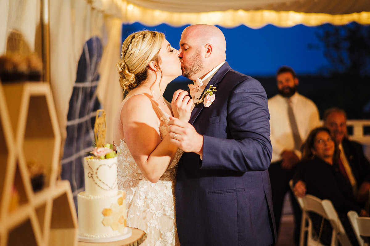 A couple embraces and kisses after cutting the cake at their Mystic, CT wedding.