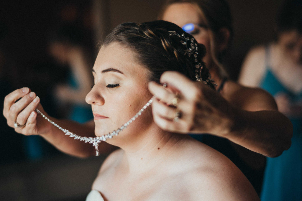 How they go about photographing details is one of the key questions to ask before hiring your wedding photographer. For example, as this mother places a diamond necklace on her bride daughter's neck, the connection is the subject rather than the jewelry.