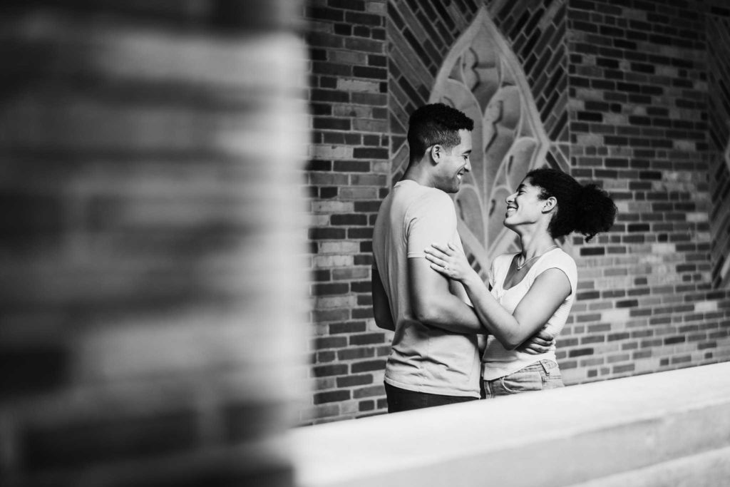 Just after their New Haven proposal, an engaged couple embraces near a brick wall during their New Haven engagement session, as taken by Connecticut wedding photographer Terrence Irving.