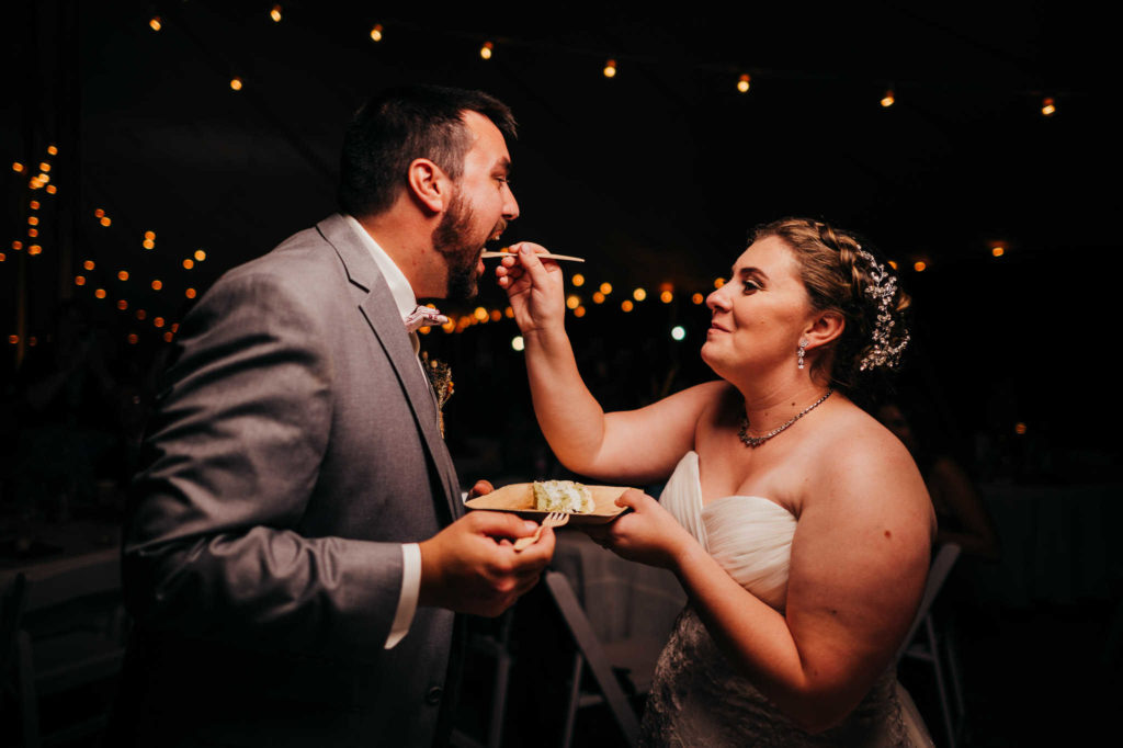 A bride feeds wedding cake to her groom. Helping couples find a great cake baker is a must for any useful Connecticut wedding guide.