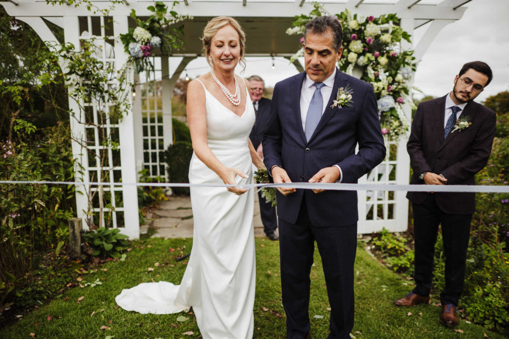 A bride and groom cut a ribbon at the end of their Stonington wedding ceremony.