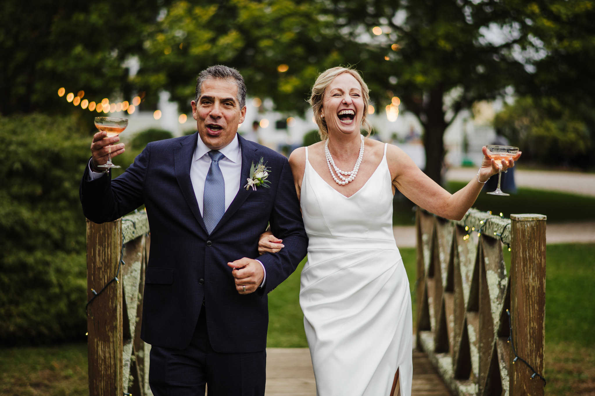 A bride and groom laugh and hold up champagne glasses at Stone Acres Farm during their Stonington wedding.