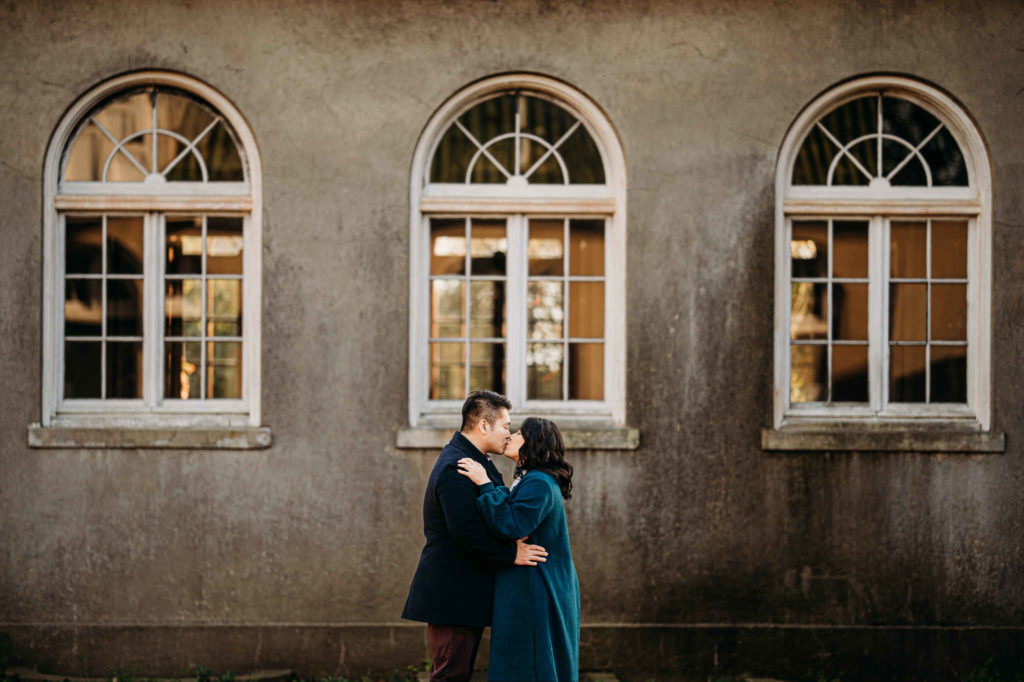 A couple stands under a window and kisses at Harkness, one of the best engagement session locations in Connecticut.