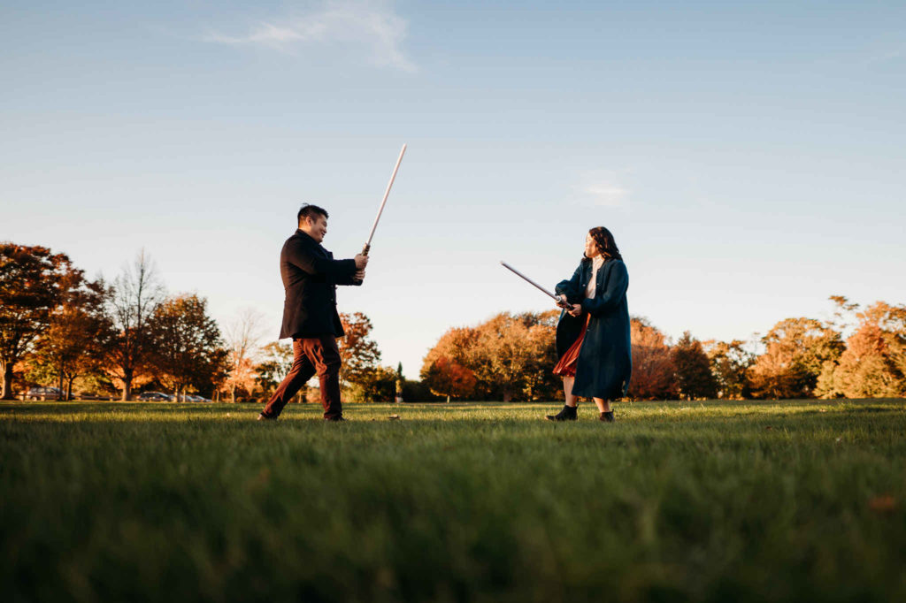 An engaged Connecticut couple mock-fights with lightsabers during their fall Harkness engagement session.