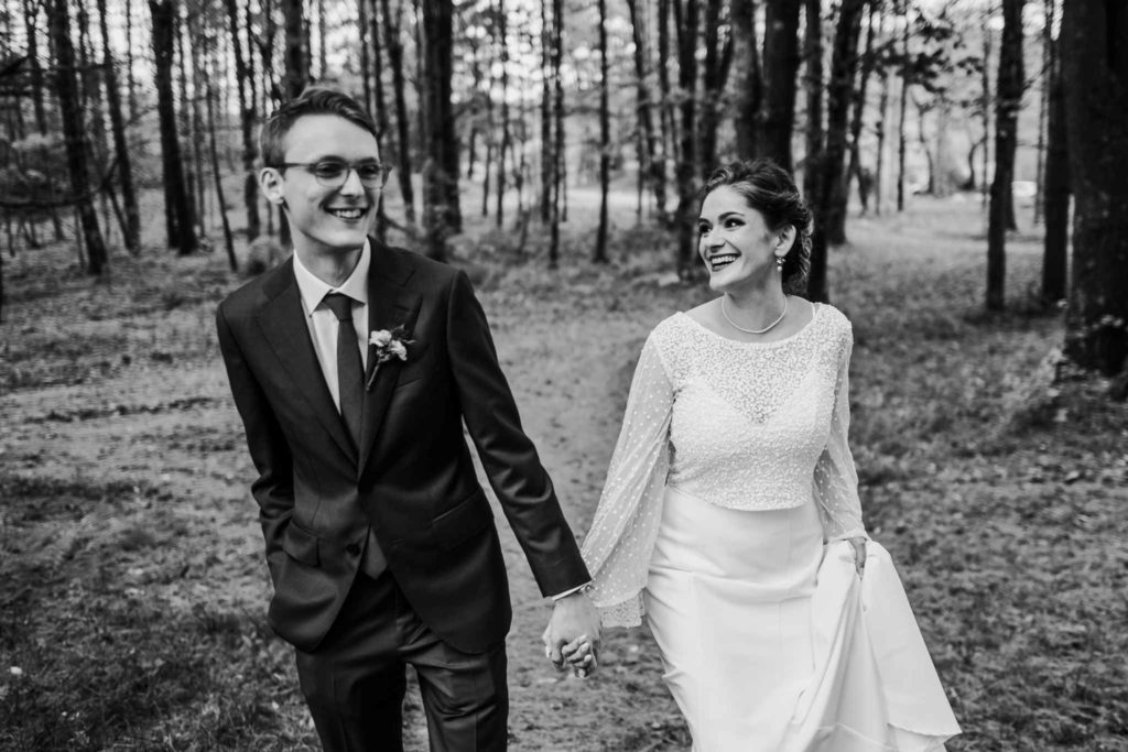 A bride and groom hold hands and walk out of a forest. Taken by Connecticut wedding photographer Terrence Irving.