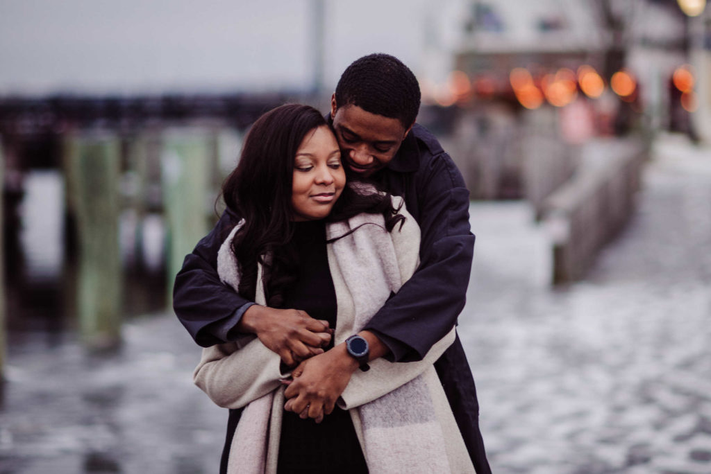 A couple hugs each other with snow on the ground in downtown Mystic, their chosen Connecticut engagement session location.