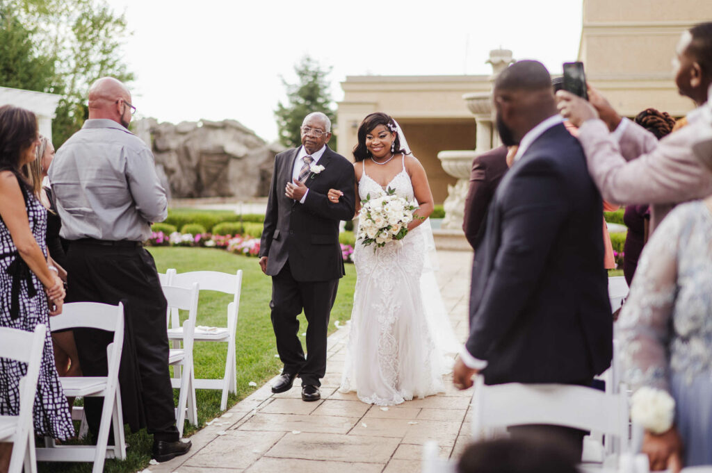 A bride is walked down the aisle by her father during her wedding at Aria wedding venue.