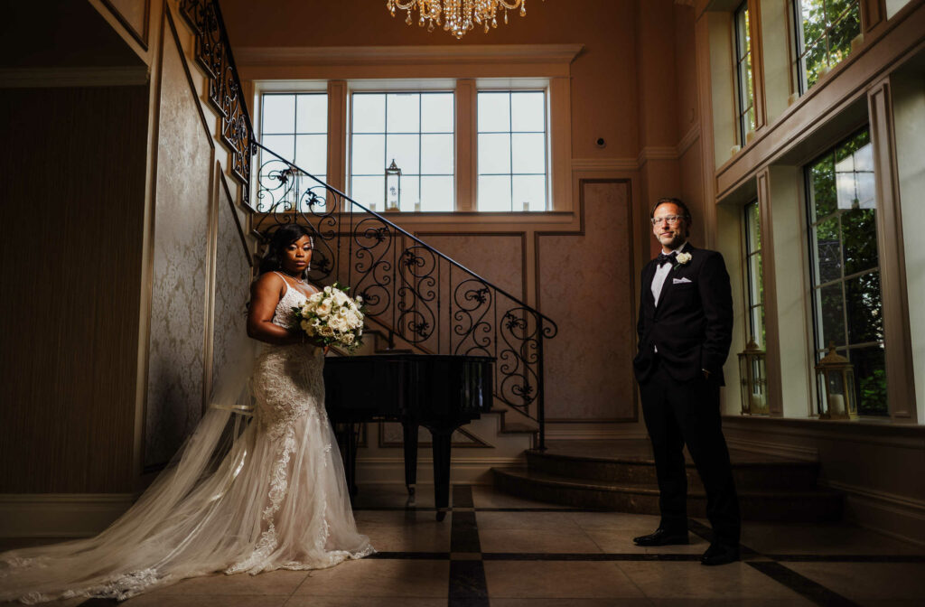 A bride and groom post in front of a piano and staircase at Aria wedding venue.