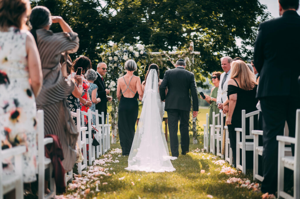 A bride is walked down the aisle by her parents during her Lion Rock Farm wedding.