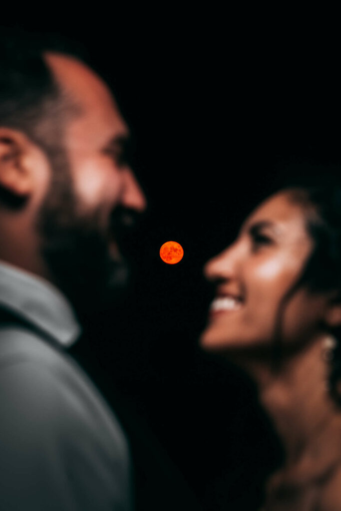 An orange moon is in the background of a bride and groom smiling at each other during their Essex CT wedding.