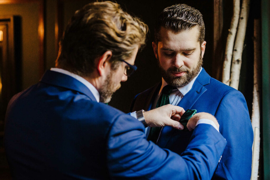 A groomsman helps the groom with his pocket square before his wedding at Lord Thompson Manor.