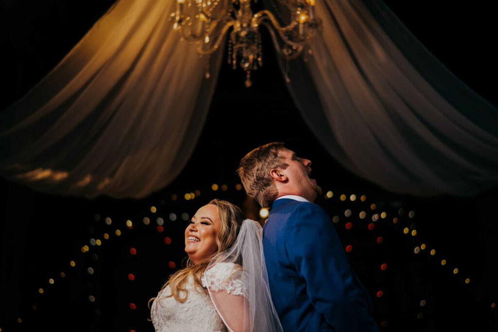 A bride and groom laugh together under a chandelier during their fall wedding at Webb barn.