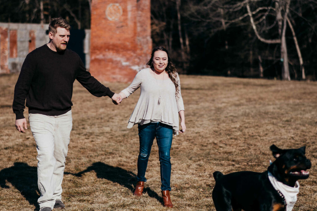 A couple walks hand in hand with their Rottweiler dog during their Glastonbury engagement session.