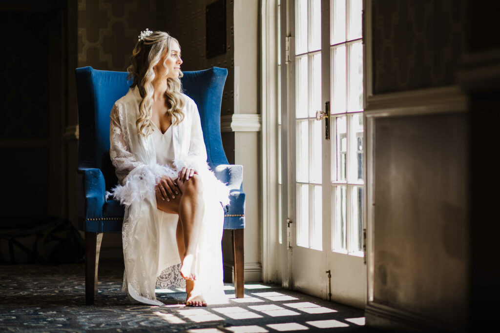 A bride poses in front of a window while sitting on a chair before her Inn at Middletown wedding.