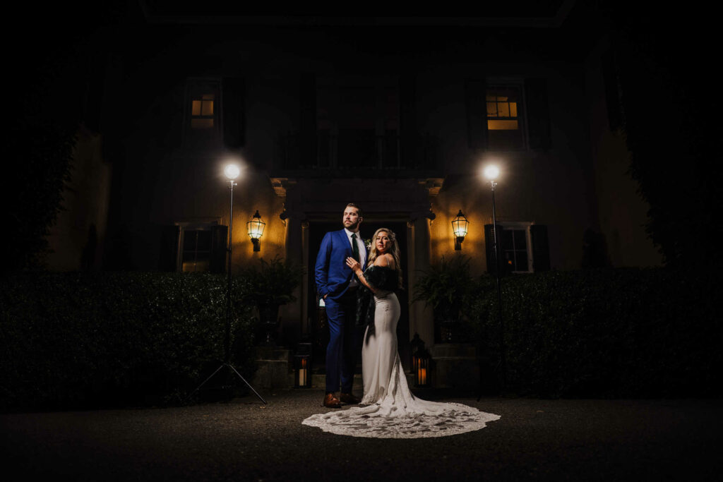 A bride and groom pose at night in front of Lord Thompson Manor in Thompson, Connecticut.