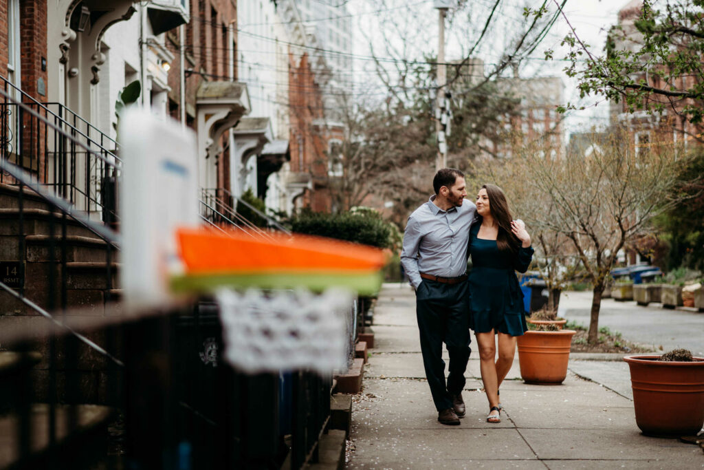 A couple walks together on a sidewalk during their New Haven engagement session near Wooster Square Park.
