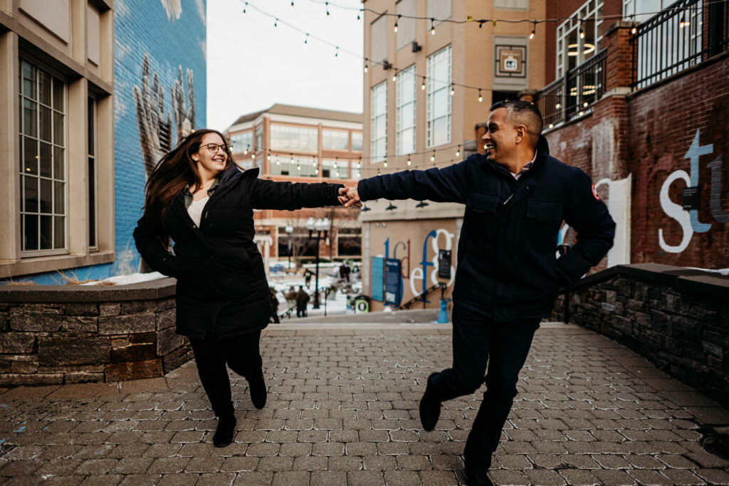 A couple holds hands and runs in Blue Back Square during their engagement session.
