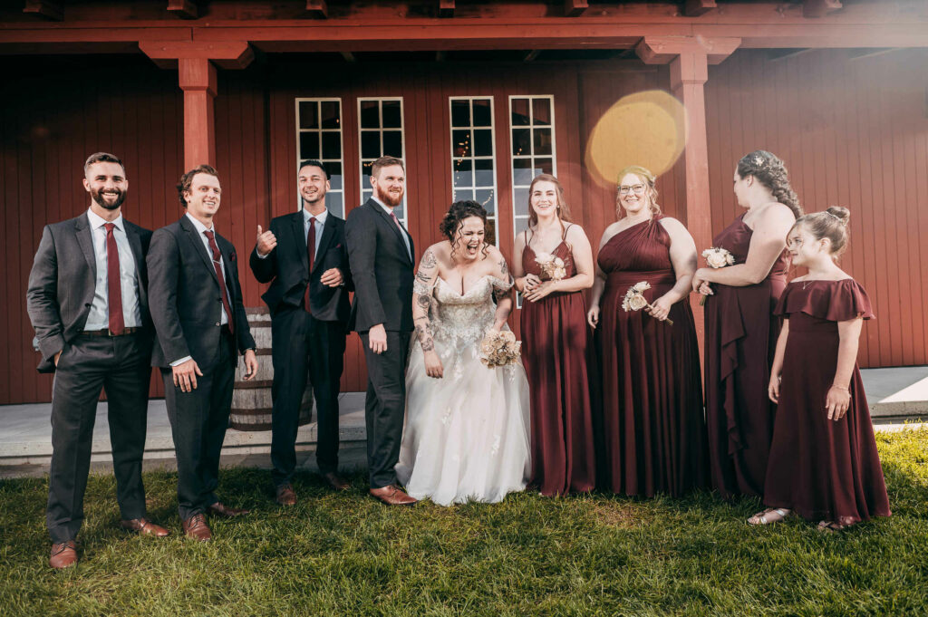 The wedding party poses, groomsmen in gray suits and bridesmaids in red dresses, during a Brooklyn barn wedding.