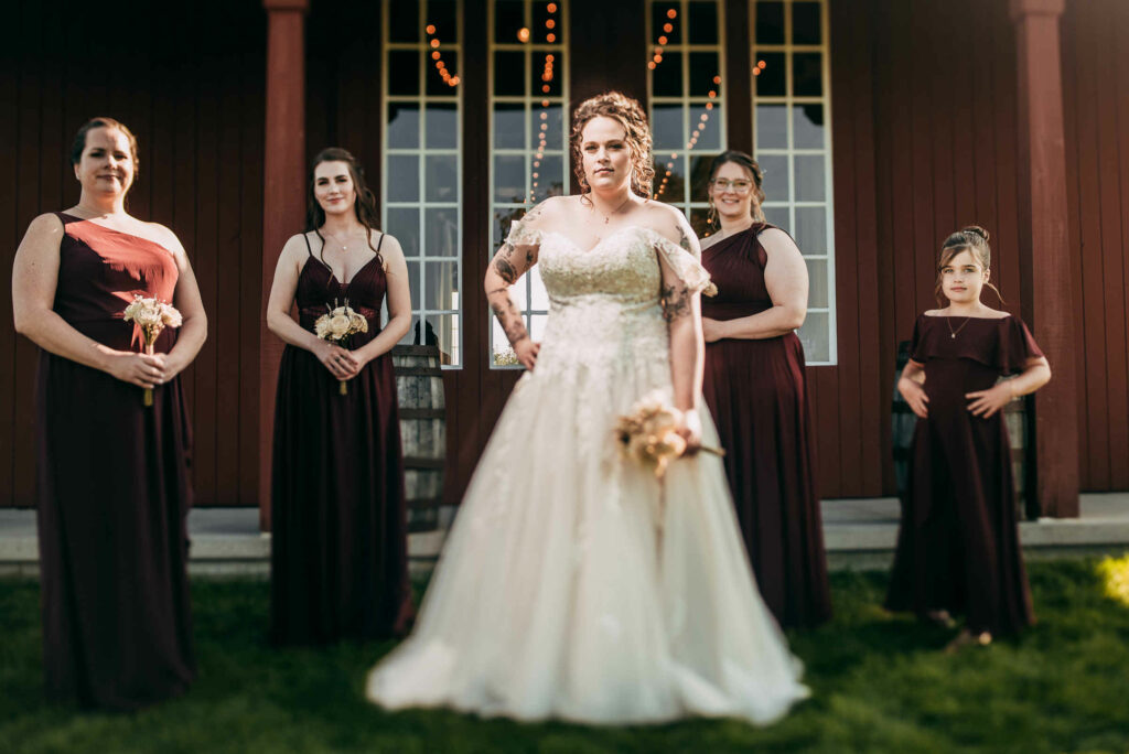 A bride and her bridesmaids stand together behind The Barn at Allen Hill Farm.