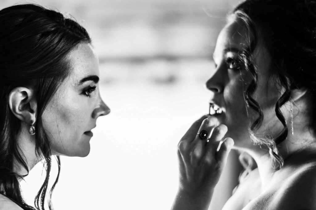 The maid of honor helps apply makeup to the bride during her Allen Hill Farm wedding.