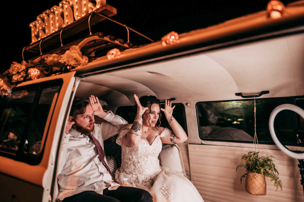A bride and groom pose inside of a vintage van converted to a photo booth during their Brooklyn barn wedding.