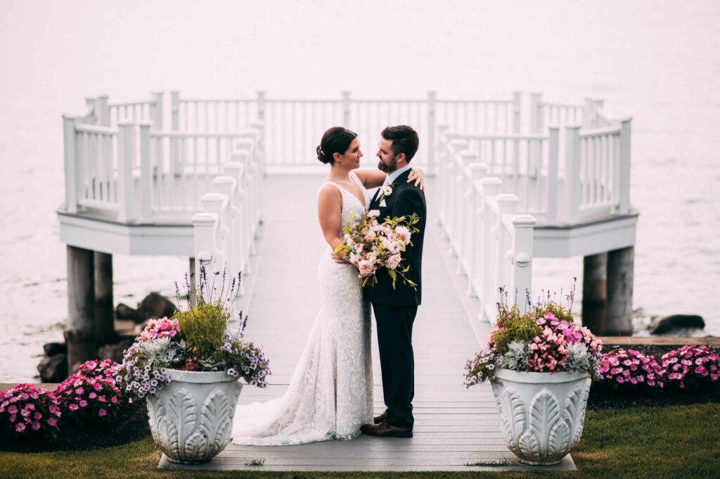 A bride and groom stand on a dock surrounded by potted flowers during their CT wedding.