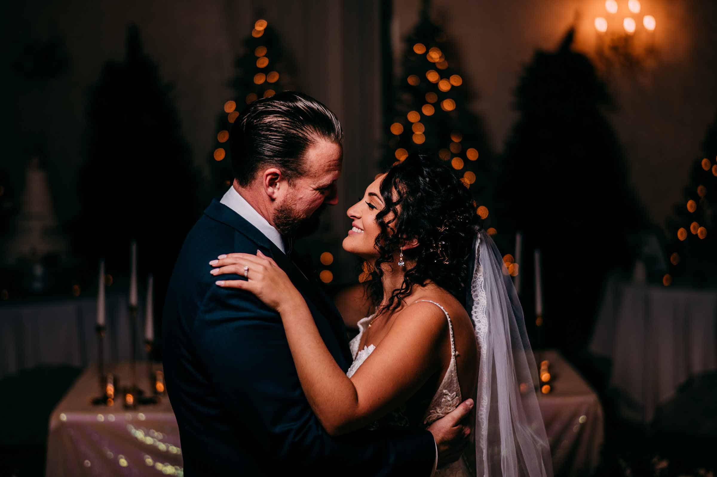 The bride and groom embrace in front of Christmas trees and their sweetheart table during their Cascade Hamden wedding.