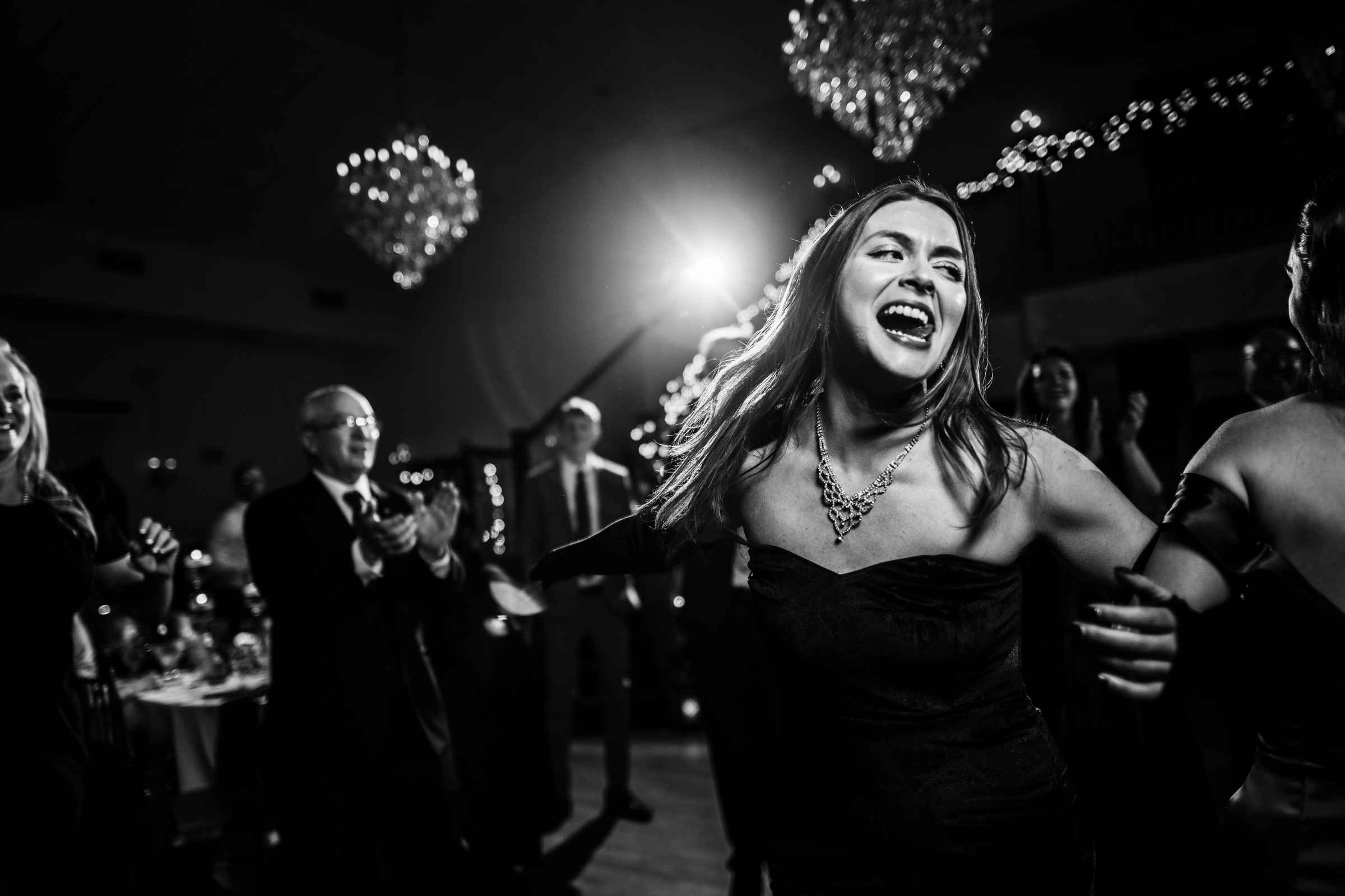 A guest dances under chandeliers in a black dress during a wedding at Cascade Fine Catering.