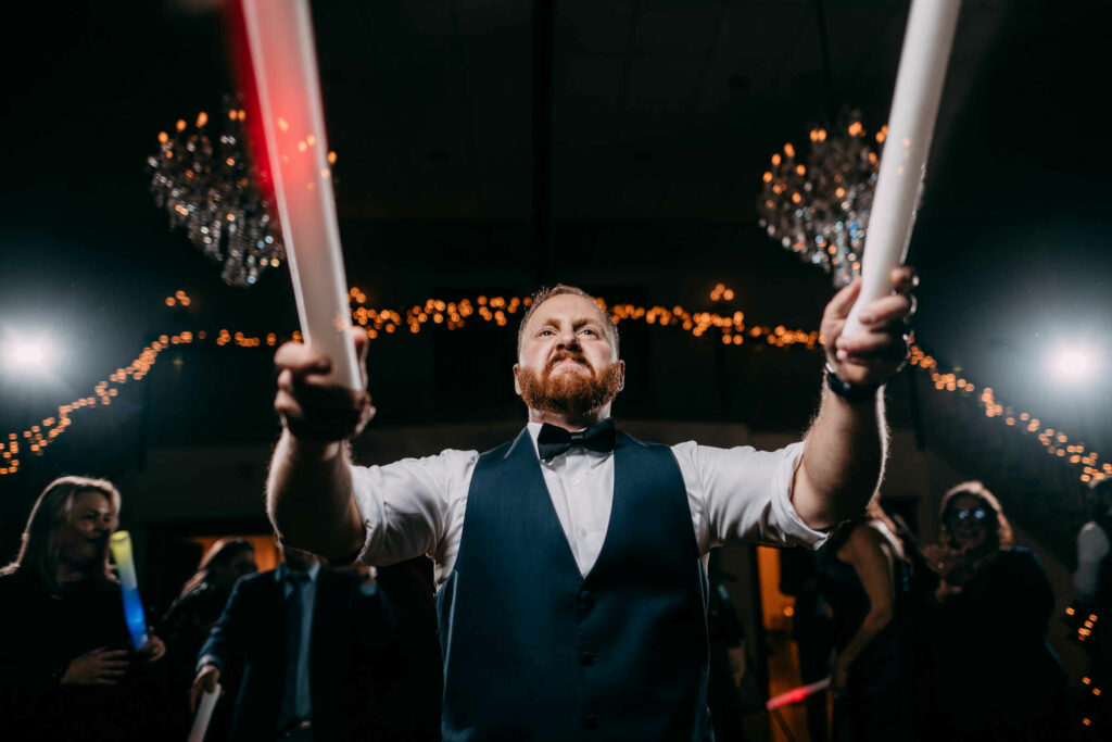 A groomsman dances with light sticks in his hands during a wedding at Cascade Fine Catering.