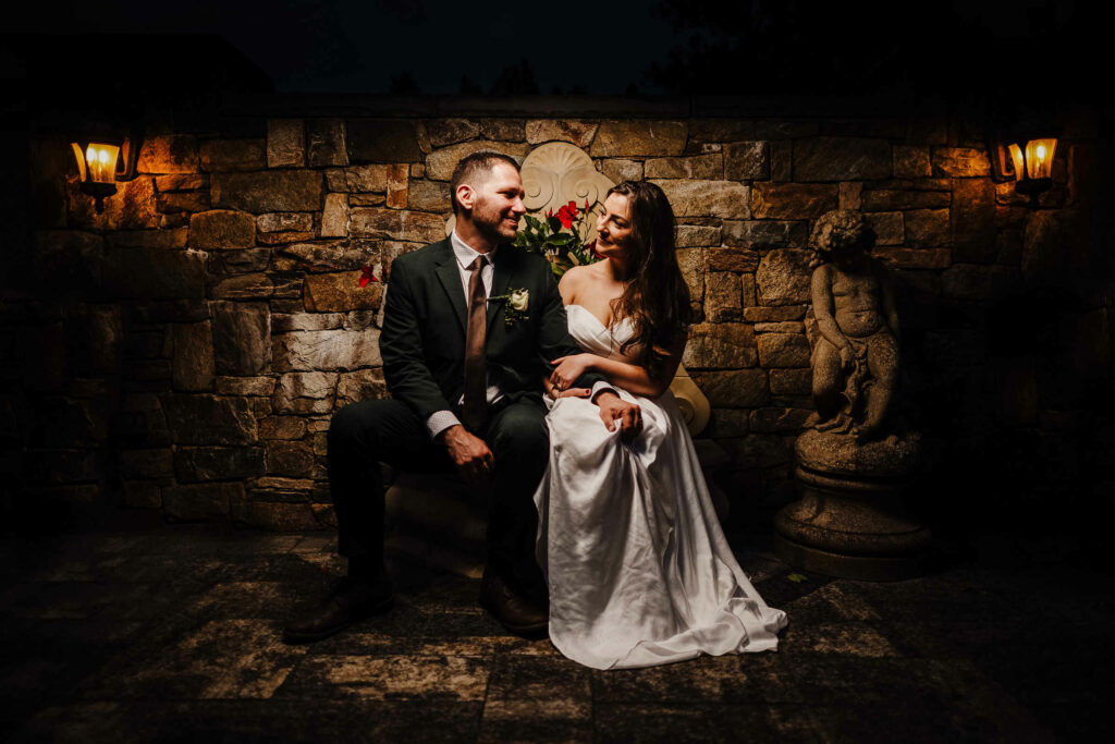 Taking at seat at night in a stone/brick garden, a bride groom are photographed by their New England wedding photographer.