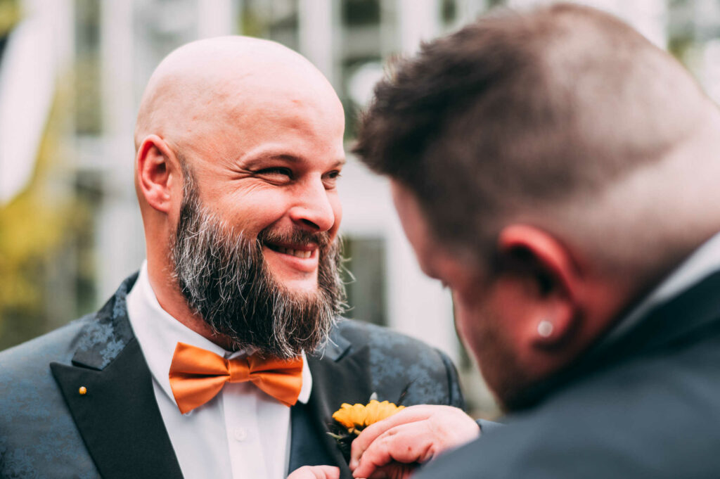 The groom smiles as his best man helps him with his boutonniere before his wedding at Roger Williams Botanical Center. 