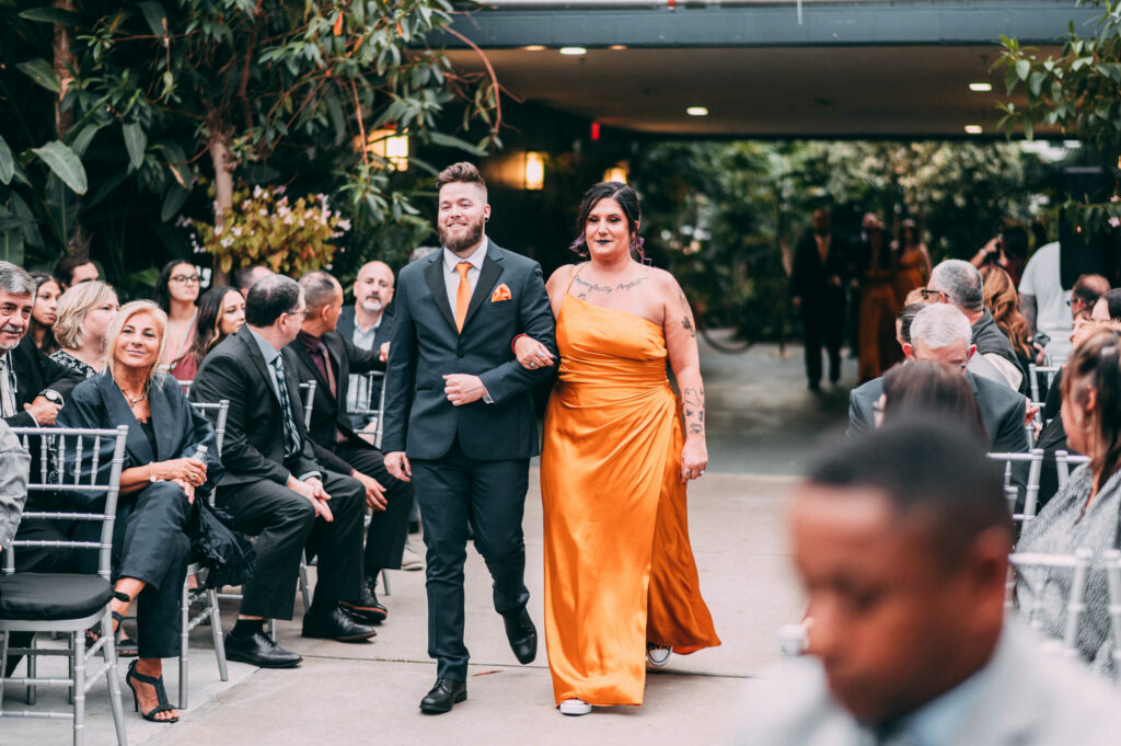 A groomsmen and bridesmaid walk into the ceremony of a Roger Williams Botanical Center wedding.