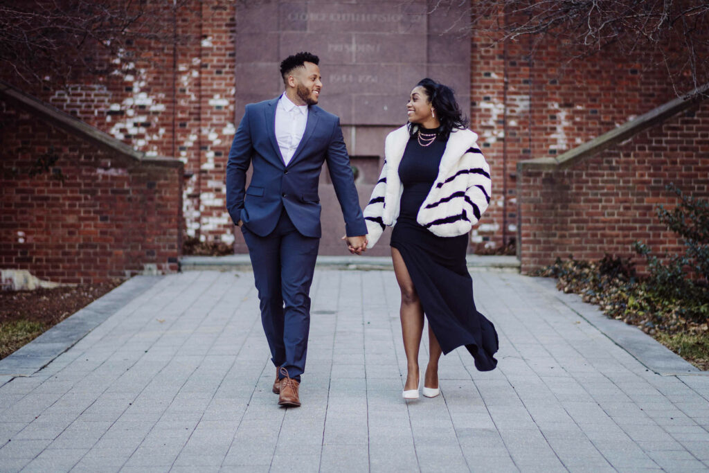 A couple holds hands while walking together during their Trinity College engagement session in Hartford CT.