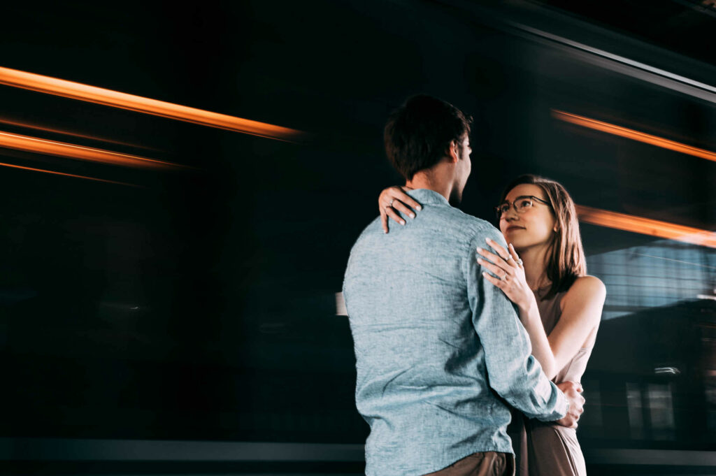 A T subway train drives by fast as an engaged couple hugs each other next to it while making Boston engagement photos.