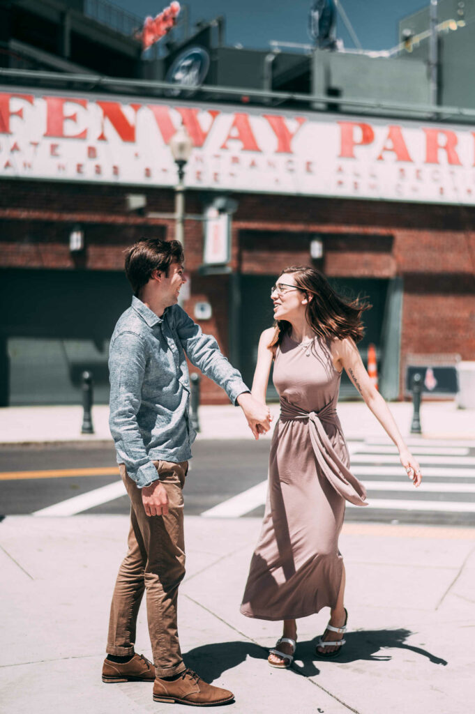 A groom-to-be twirls his fiancé in front of Fenway Park while taking their Boston engagement photos.