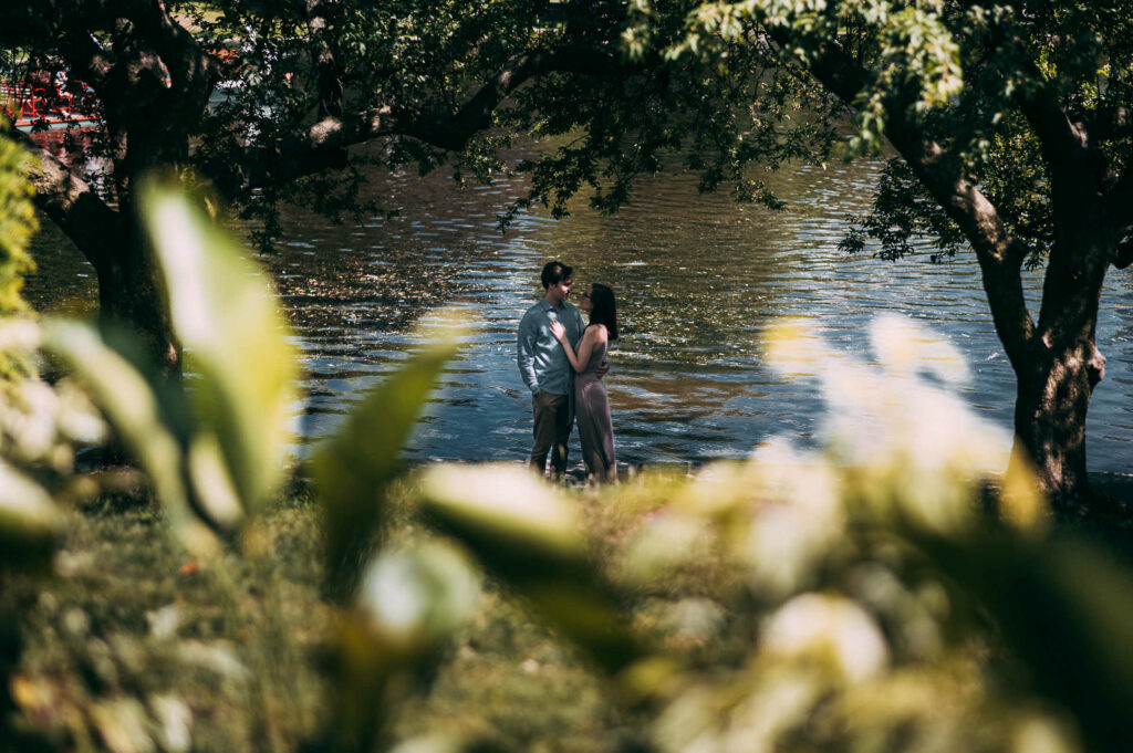 For one of their Boston engagement photos, a couple stands by the pond at Boston Public Garden and the bride-to-be rests her hand on her partner's chest.