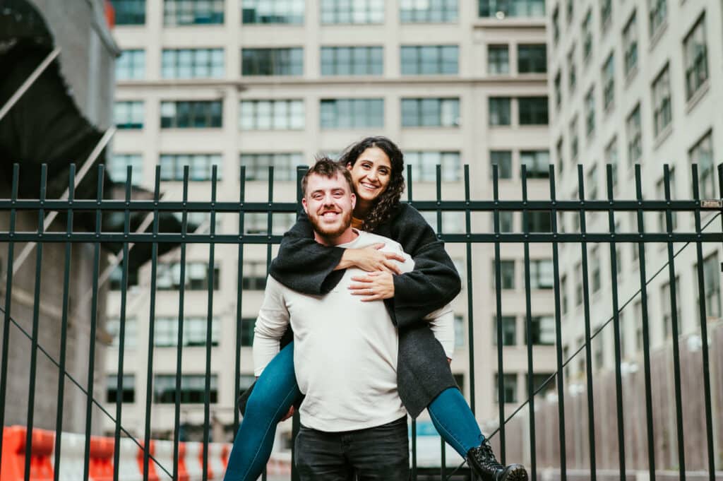 A groom-to-be holds his fiancé on his back as they both smile during their Brooklyn engagement session.