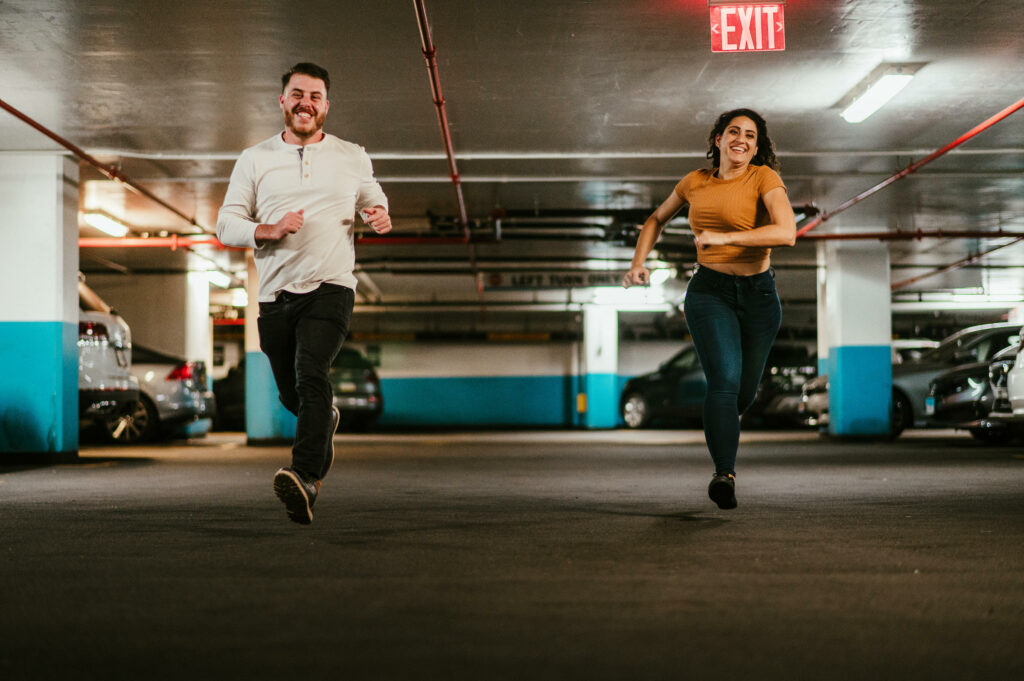 In a parking garage, a couple races each other during their Brooklyn engagement session.