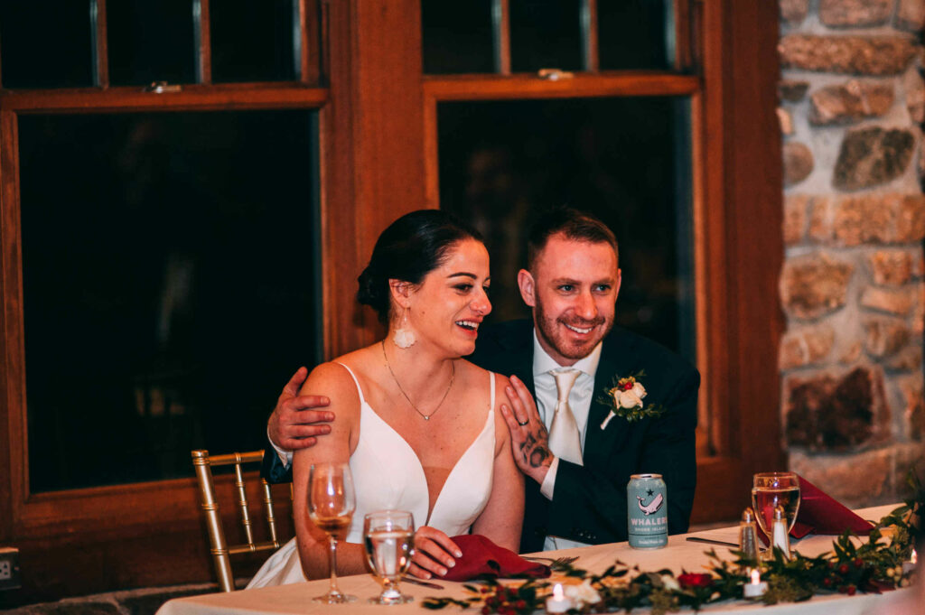A bride and groom sit at their sweetheart table and enjoy a laugh during their Towers Rhode Island wedding.
