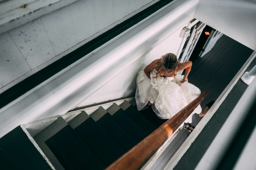 A bride walks up green carpeted stairs to her Madison CT wedding first look.