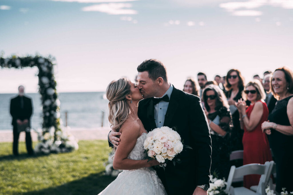 A couple kisses in the center aisle of their wedding at Madison Beach Club.