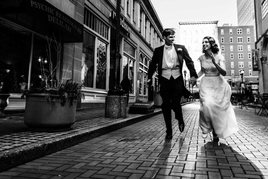 A wedding couple in elegant attire holds hands and runs down Pratt Street during their Society Room of Hartford wedding.