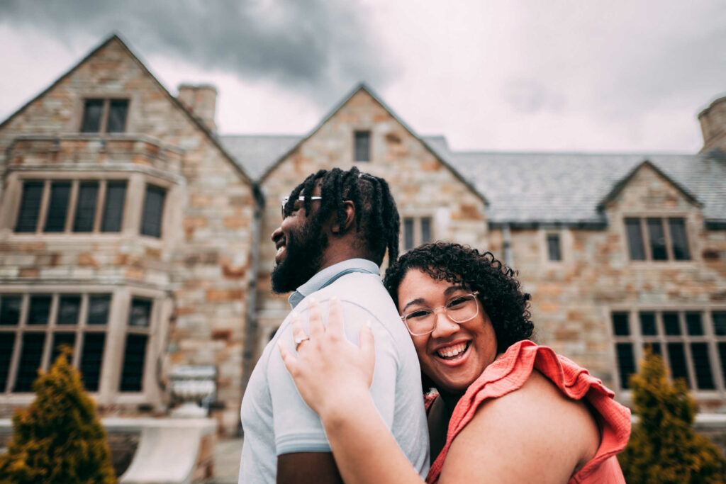 A black couple poses together in front of Gallaher Mansion at Cranbury Park during their engagement session.